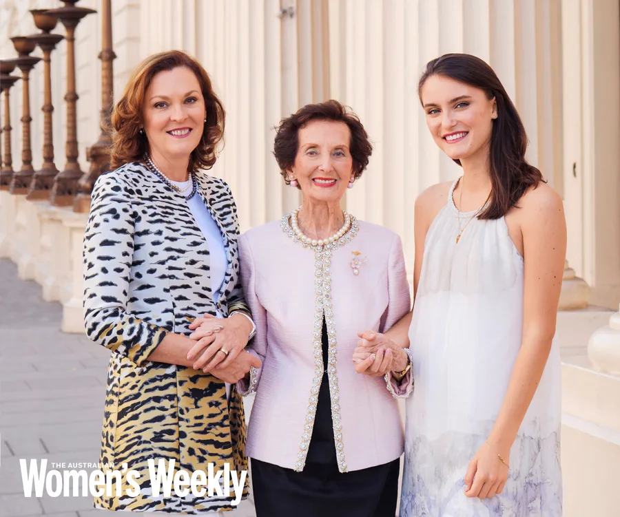Three women smiling, standing arm-in-arm in front of a classical building.