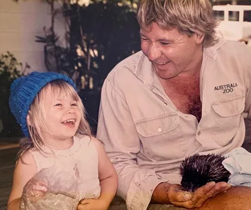 Father and daughter smiling together, with father holding a small animal; he is wearing an Australia Zoo shirt.