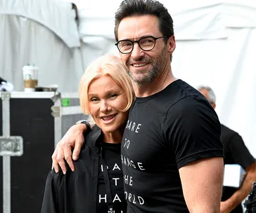 Couple smiling together at an event, both in black t-shirts, with the man wearing glasses.