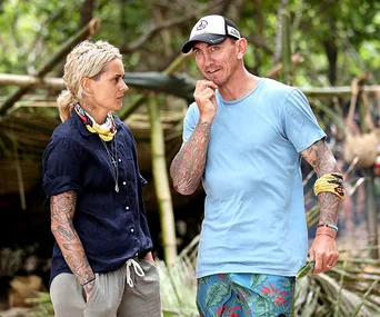Two contestants from Survivor 2020 have a conversation at camp, surrounded by natural foliage.