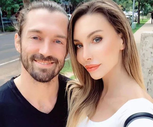 Man with a beard and woman with long hair taking a selfie outdoors, both smiling.