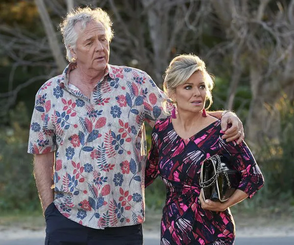 Two characters from "Home and Away," John and Marilyn, standing together outside, looking concerned.