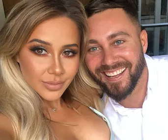 A smiling couple takes a close-up selfie indoors, with a woman on the left and a man on the right.