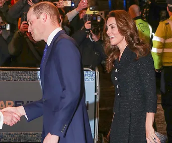 Prince William and Kate Middleton greet attendees at a theater event, surrounded by photographers.