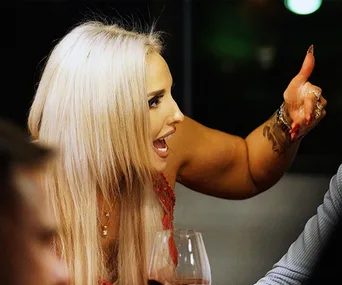 A woman with long blonde hair, gesturing passionately, holding a wine glass.