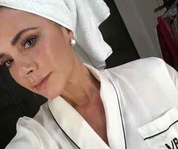 A woman in a white bathrobe with a towel wrapped around her head, wearing square earrings.