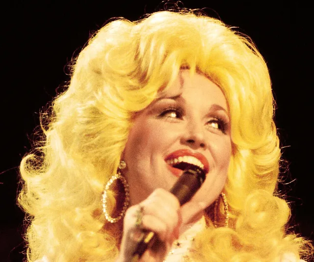 Singer with bright blonde hair and a microphone, smiling on stage.