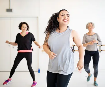 Women smiling and dancing in a bright fitness studio.
