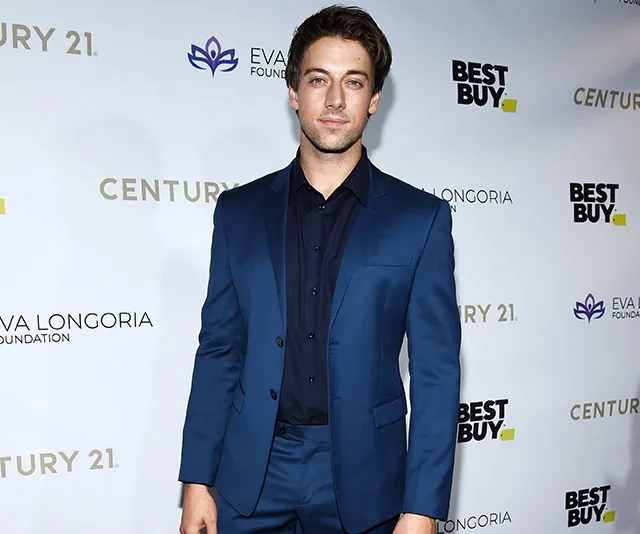 Actor in a blue suit at a red carpet event with sponsor logos, including Best Buy and Century 21, on the backdrop.
