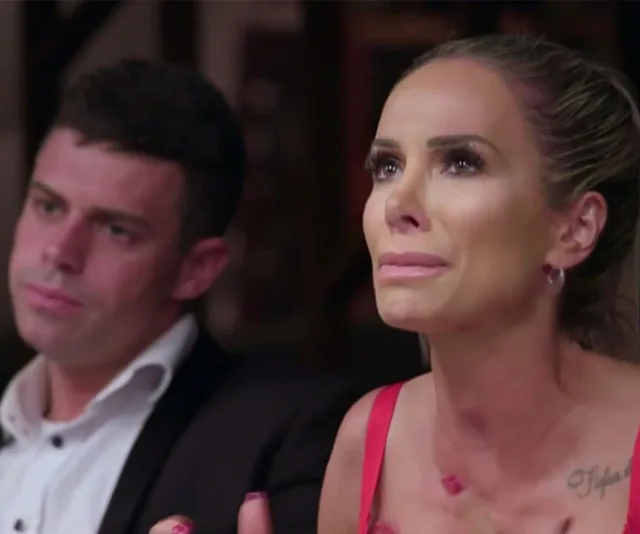 Stacey and another person from "MAFS" sitting, Stacey appears emotional, wearing a red outfit.