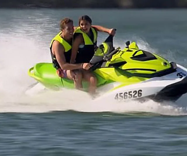 A couple wearing life vests rides a green jet ski, smiling and enjoying their time on the water.