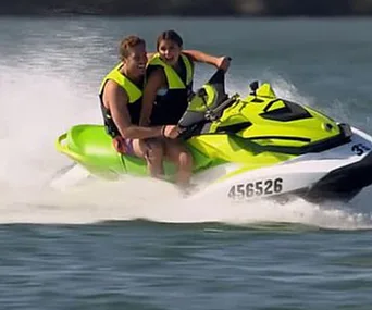 A couple wearing life vests rides a green jet ski, smiling and enjoying their time on the water.