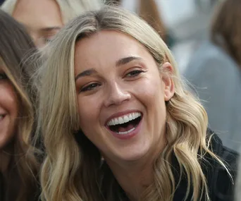 A woman with long blonde hair laughing joyfully in a crowd.