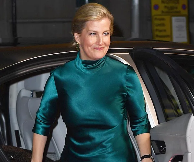 A woman in a green silk dress exits a car, smiling.