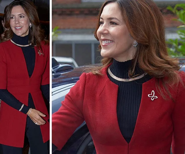 A woman wearing a red jacket and black top, smiling and standing near a car.