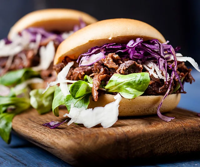 Pulled jackfruit sandwiches with lettuce and shredded red cabbage on a wooden board.