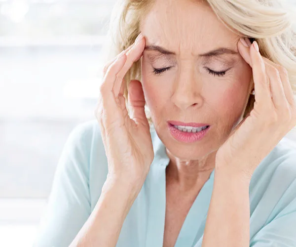 A woman with closed eyes and hands on her temples, appearing to have a headache.