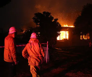 Firefighters battling a house fire at night, with flames visible through windows in Batlow.