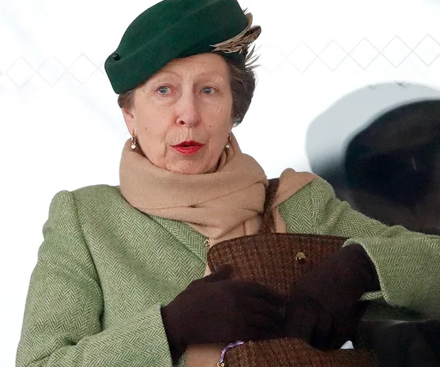 Woman in a green coat and hat with a beige scarf and gloves, sitting and holding a bag.