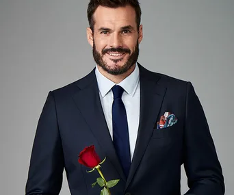 Man in a suit holding a red rose, smiling.