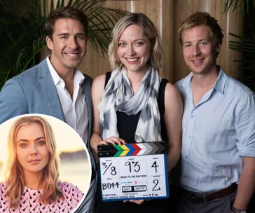 Actors posing with a clapperboard on the "Back to the Rafters" set, inset photo of a smiling woman.