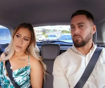 Two people sitting in the backseat of a car, wearing seatbelts and looking forward.