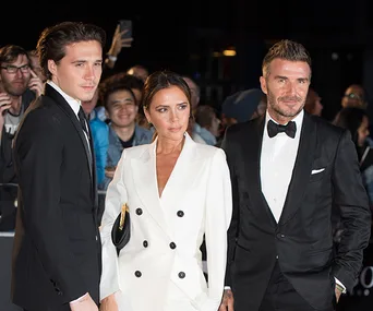 Brooklyn, Victoria, and David Beckham dressed elegantly at a formal event with a crowd in the background.