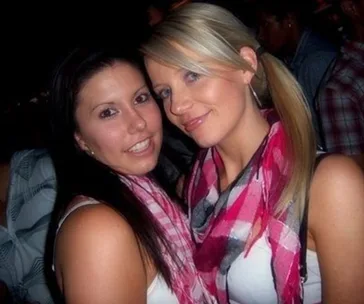 Two women smiling, wearing pink checkered scarves at a social event.