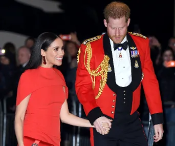 Couple in formal attire, woman in red dress, man in red military uniform, holding hands and walking.