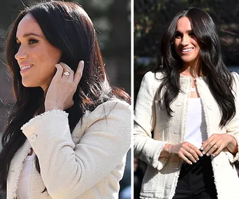 Meghan Markle smiling, wearing a white jacket and dark pants, outdoors during International Women's Day event.