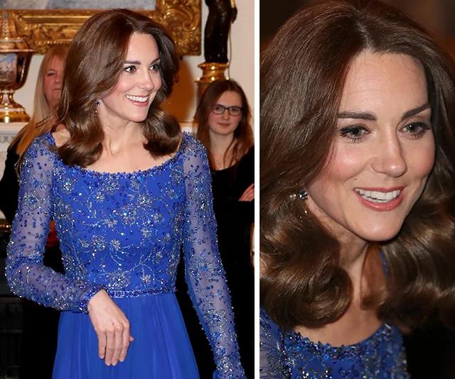 A woman in an elegant blue dress adorned with sequins, smiling at an indoor event.