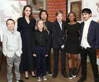 Group photo with Angelina Jolie and six children, elegantly dressed, standing together and smiling indoors at an event.