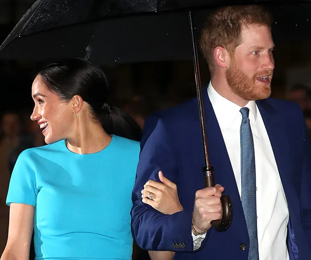 Couple smiling under an umbrella at an evening event.