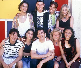 A group of nine teenagers, smiling, posed together in front of a colorful wall.