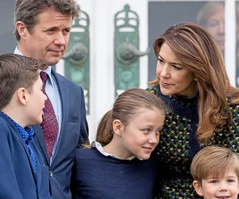 A family of five, including two adults and three children, standing closely together outdoors, smiling and interacting.