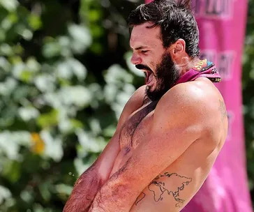 Man with beard and tattoos shouting energetically during an outdoor challenge on Survivor.
