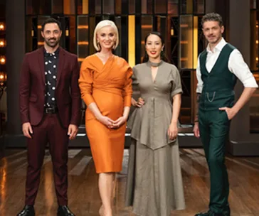 Group of four judges standing on the MasterChef set, dressed in stylish formal attire.