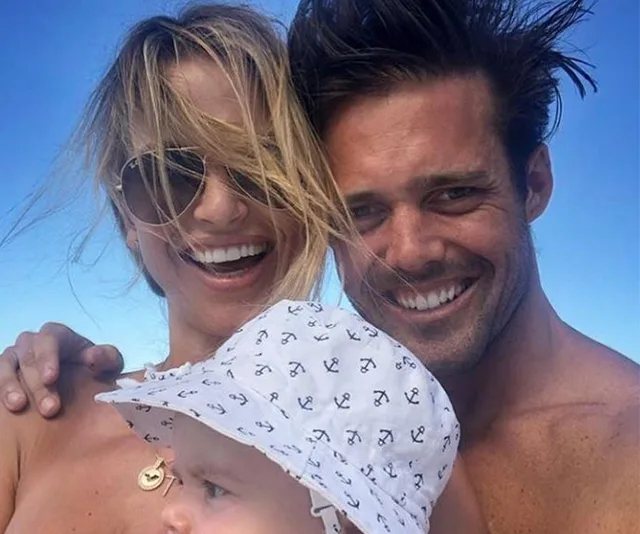 A smiling couple with a baby in a sun hat, enjoying a sunny day outdoors.