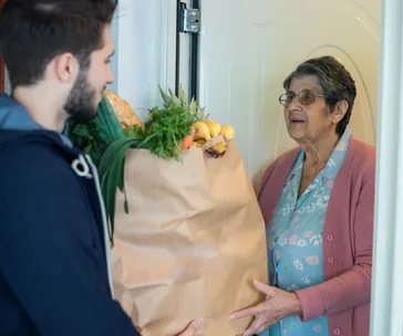 A young man delivers groceries to an elderly woman at her door.