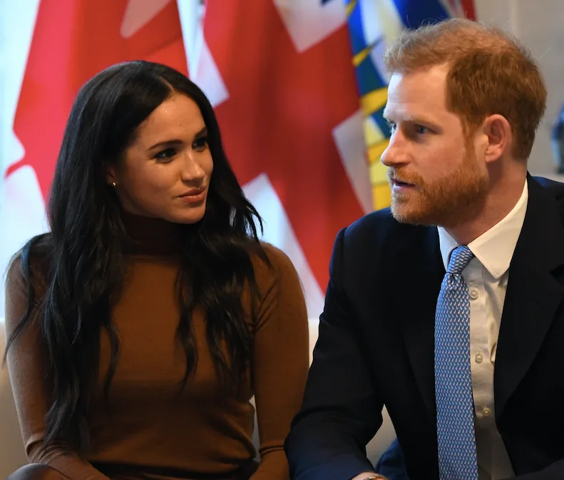 A man and woman are seated and engaged in conversation, with flags visible in the background.