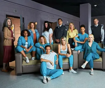 Cast of "Wentworth" in prison setting, actors in blue uniforms and guards in black, posed in common area.