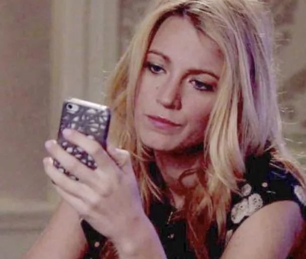 A woman with long blonde hair looks intently at her phone while sitting indoors.