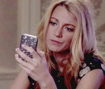 A woman with long blonde hair looks intently at her phone while sitting indoors.