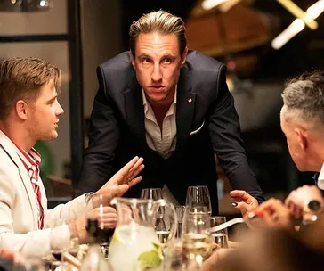 Men in formal attire conversing intensely around a dinner table.