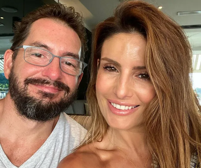 A man with glasses and a woman with long hair smiling for a selfie indoors.