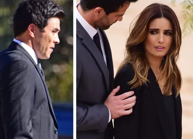 Two people are conversing seriously outdoors, while another person is walking away in a suit.