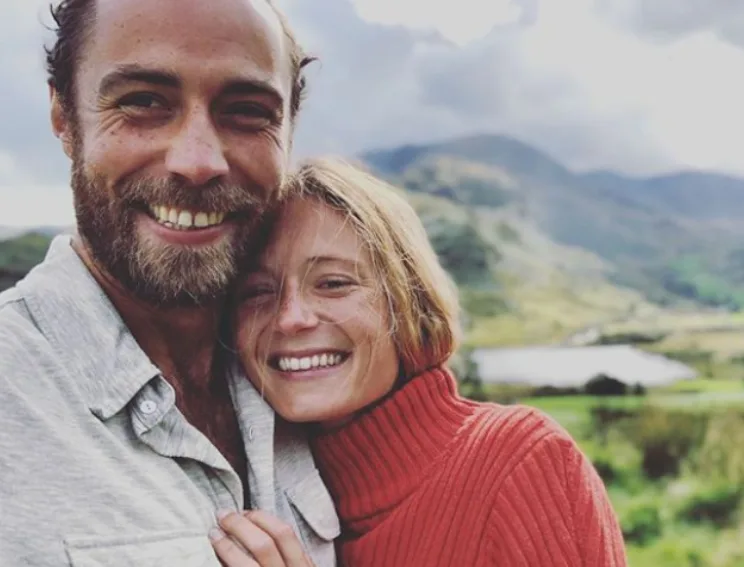 Couple smiling together outdoors in a scenic landscape with mountains in the background.