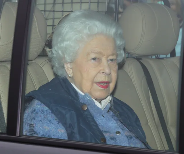 Older woman with short white hair sitting in a car, wearing a blue outfit, visible through the car window.