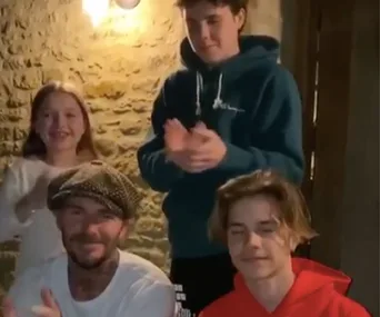 Family clapping hands indoors, smiling, with stone wall background.
