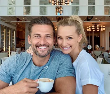 A smiling couple in a cafe, the man holding a coffee cup, sitting close together.
